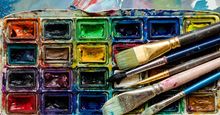 Artist paint brushes and watercolor paintbox on wooden palette. Instruments and tools for creative leisure. Creative background. Paintings art concept. Painting hobby. Back to school. Top view.