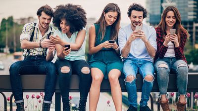 Multi-ethnic group of people sitting on an urban bridge text messaging and sharing smart phone content.